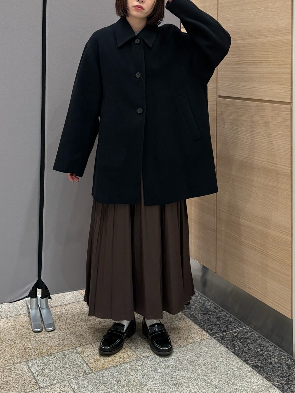 ブラック系のステンカラーコート、ブラウン系のスカート、グレー系のニット/セーターを着用したレディースの秋コーディネートの3枚目の写真
