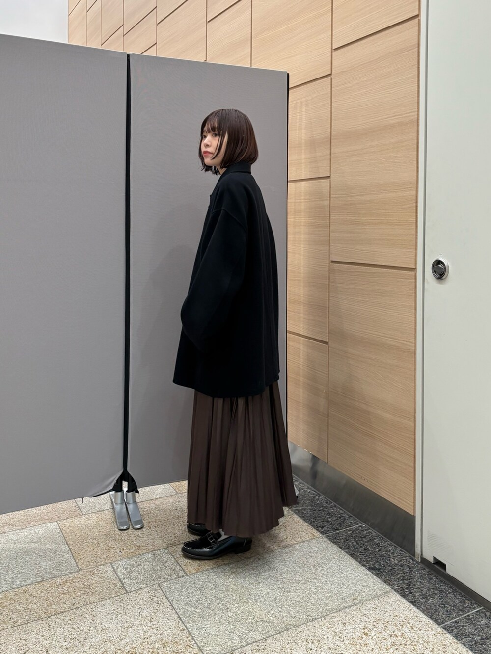 ブラック系のステンカラーコート、ブラウン系のスカート、グレー系のニット/セーターを着用したレディースの秋コーディネートの2枚目の写真