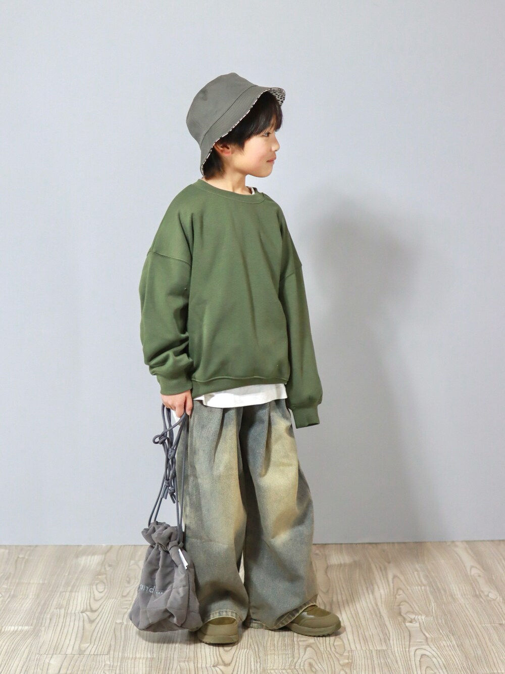 グリーン系のスウェット、ブルー系のデニムパンツ、グレー系のハンドバッグを着用したキッズの冬コーディネートの2枚目の写真