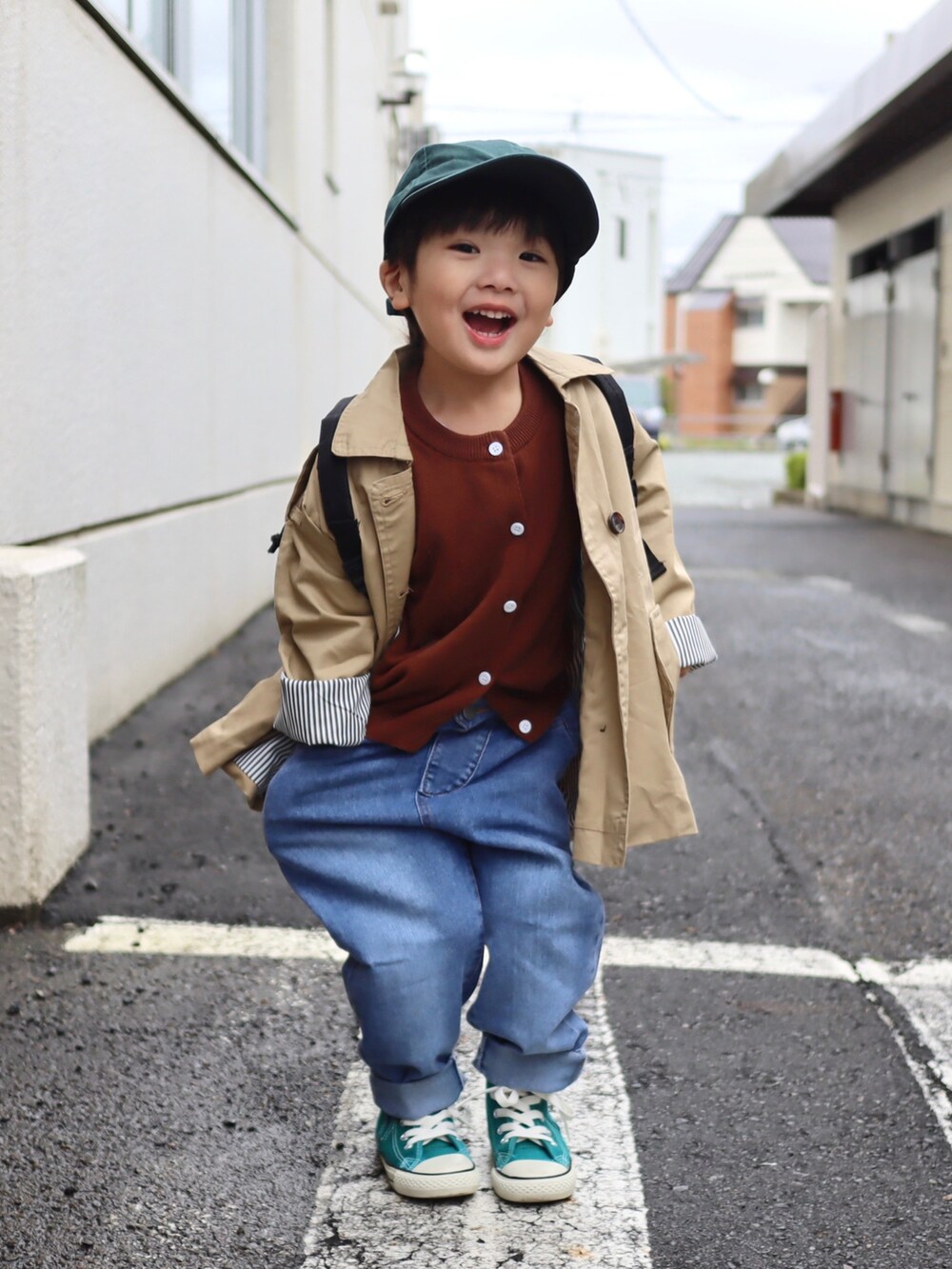 ブルー系のデニムパンツ、ベージュ系のトレンチコート、グリーン系のスニーカーを着用したキッズの秋コーディネートの2枚目の写真