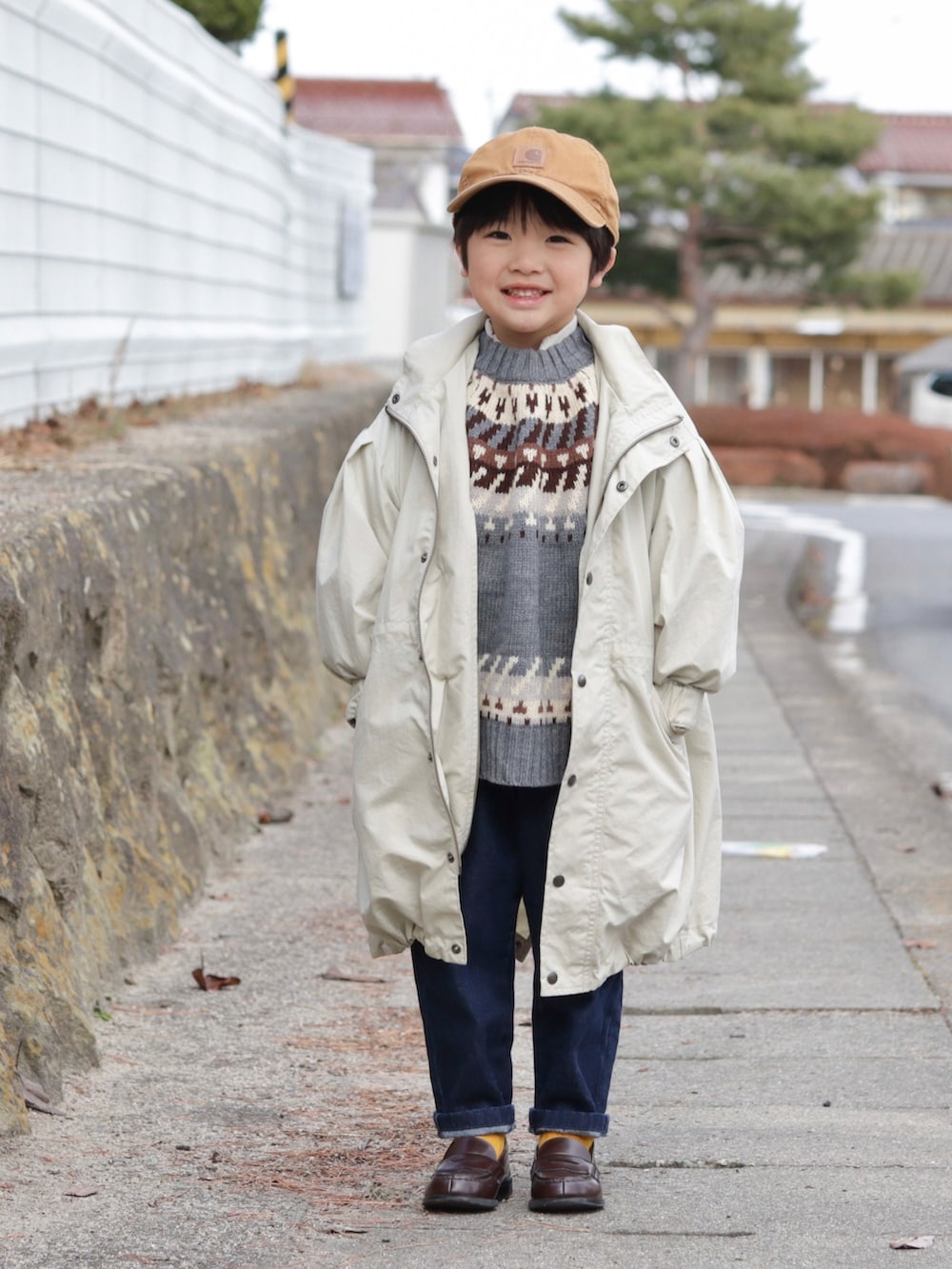 ベージュ系のモッズコート、グレー系のニット/セーター、ブルー系のデニムパンツを着用したキッズの冬コーディネートの2枚目の写真