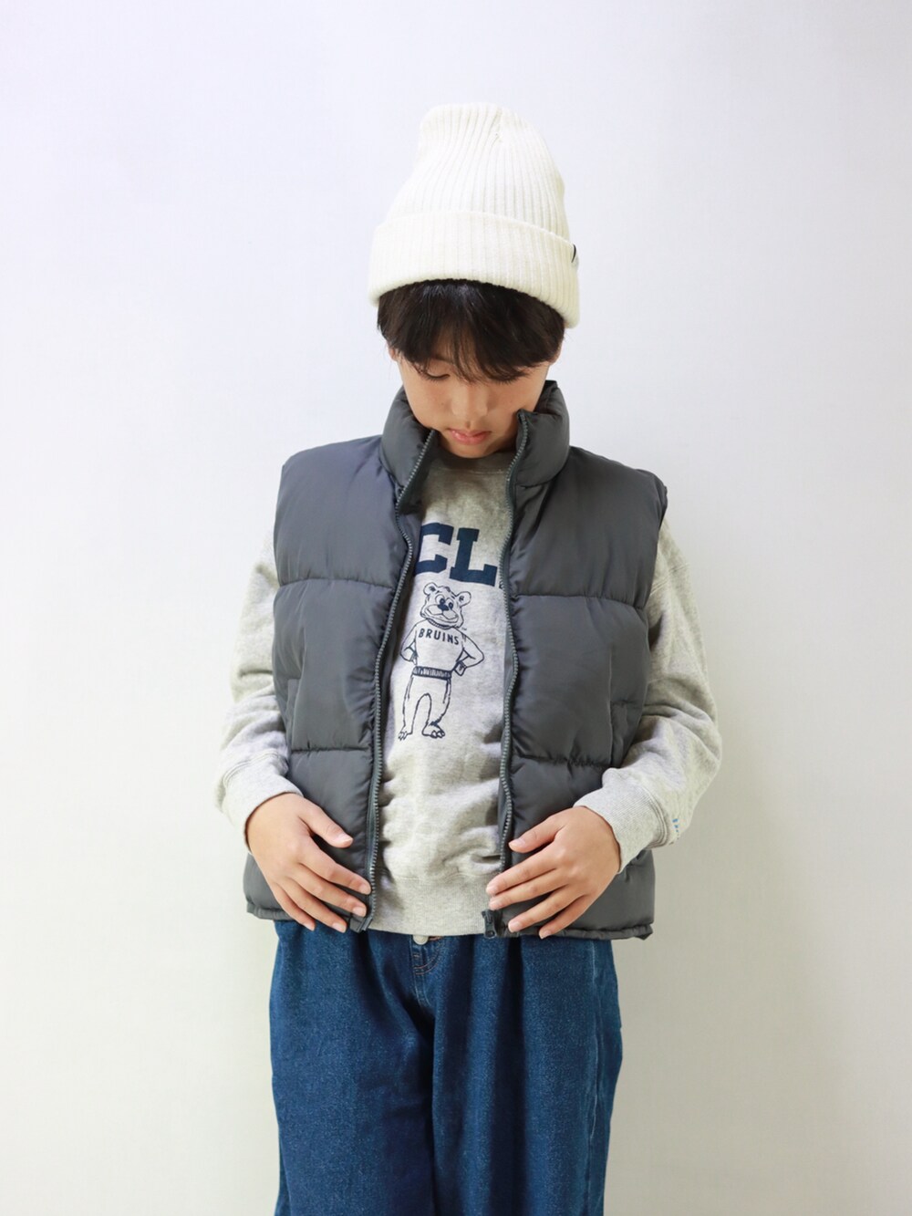 ホワイト系のスウェット、グレー系のダウンベスト、ブルー系のデニムパンツを着用したキッズの冬コーディネートの2枚目の写真