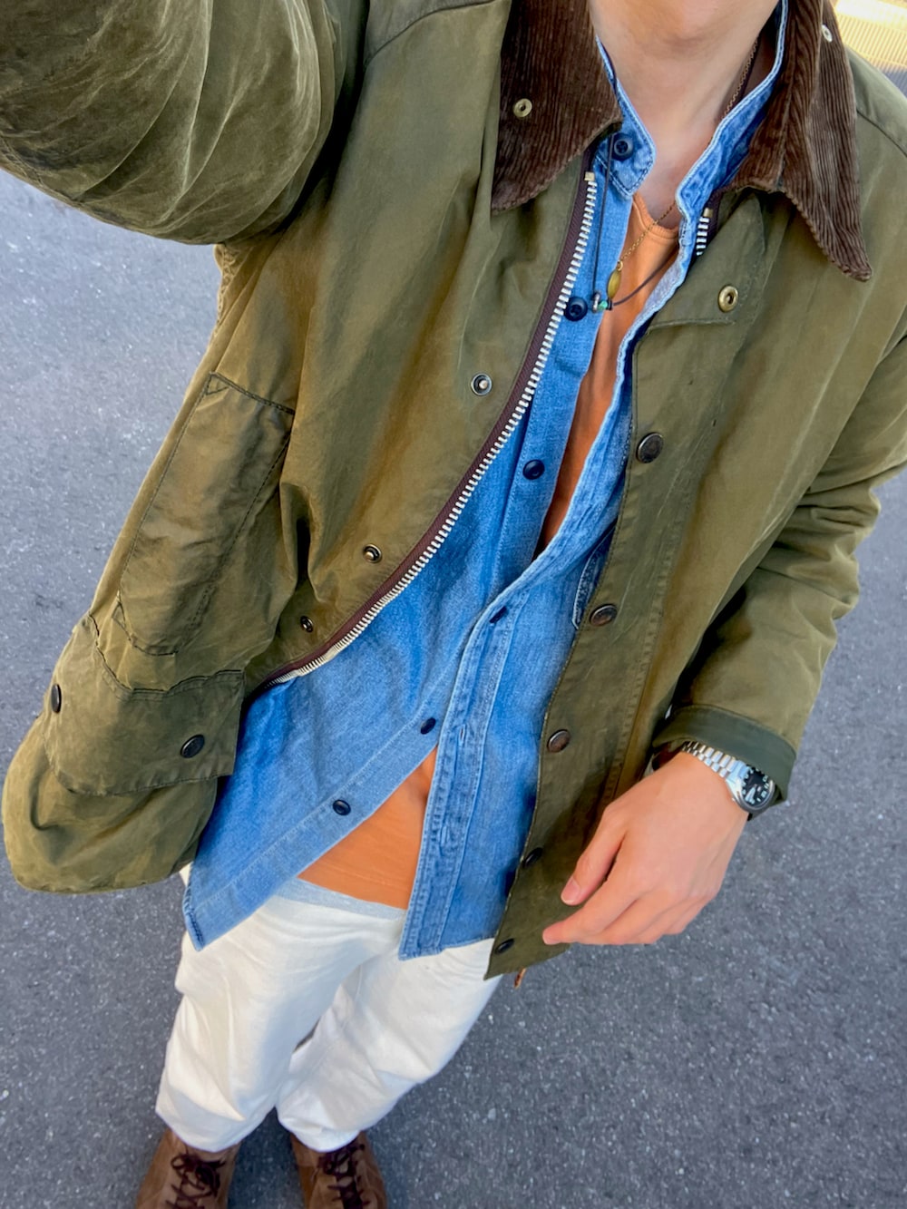 グリーン系のダウンベスト、ブラウン系のスニーカー、オレンジ系のTシャツ/カットソーを着用したメンズの冬コーディネートの2枚目の写真