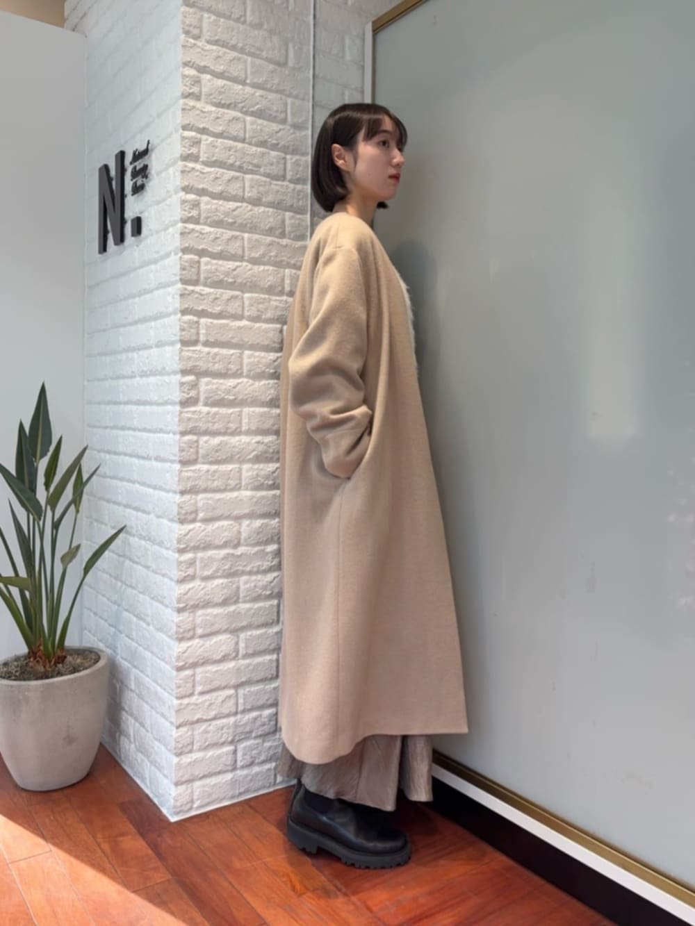 ベージュ系のノーカラーコートを着用したレディースの冬コーディネートの2枚目の写真