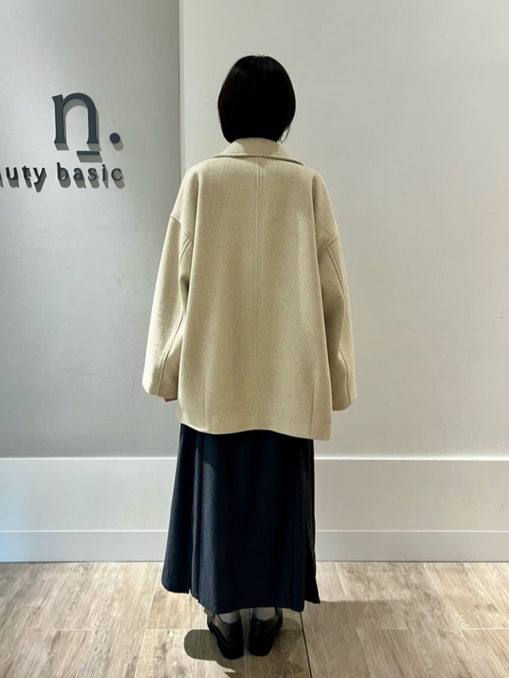 ベージュ系のピーコート、グレー系のニット/セーター、グレー系のスカートを着用したレディースの秋コーディネートの2枚目の写真