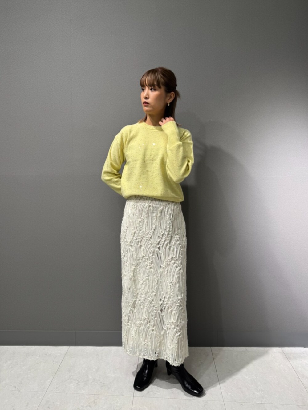 ブラック系のブーツ、ブラック系のチェスターコート、イエロー系のニット/セーターを着用したレディースの冬コーディネートの2枚目の写真