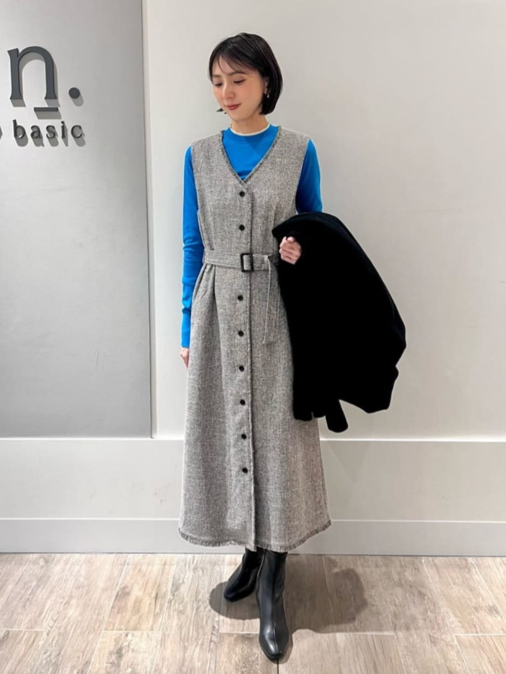 グレー系のジャンパースカート、ブルー系のニット/セーター、ブラック系のチェスターコートを着用したレディースの冬コーディネートの2枚目の写真