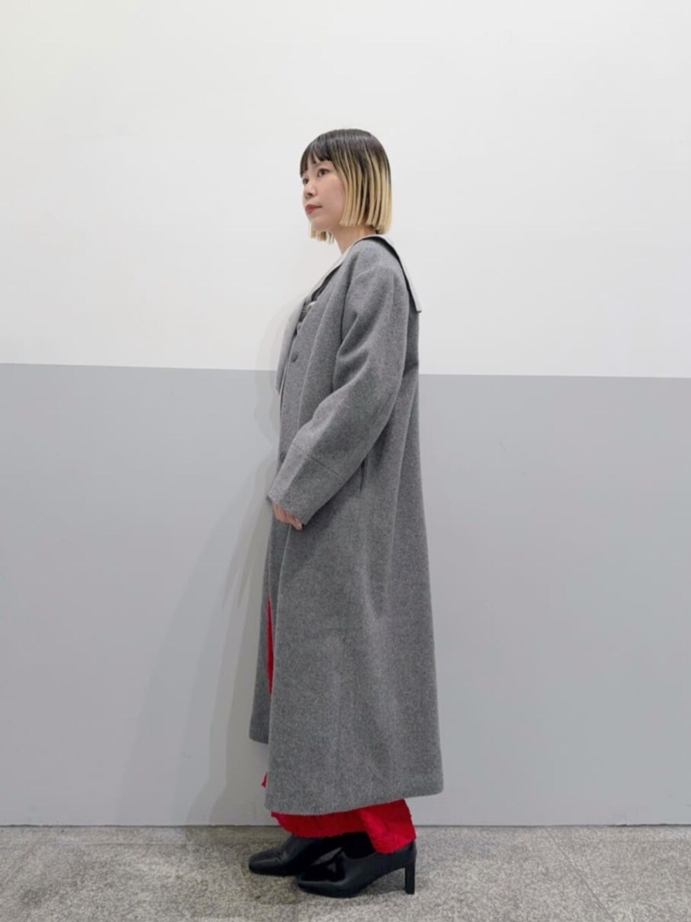 レッド系のスカート、グレー系のノーカラーコート、グレー系のニット/セーターを着用したレディースの冬コーディネートの2枚目の写真