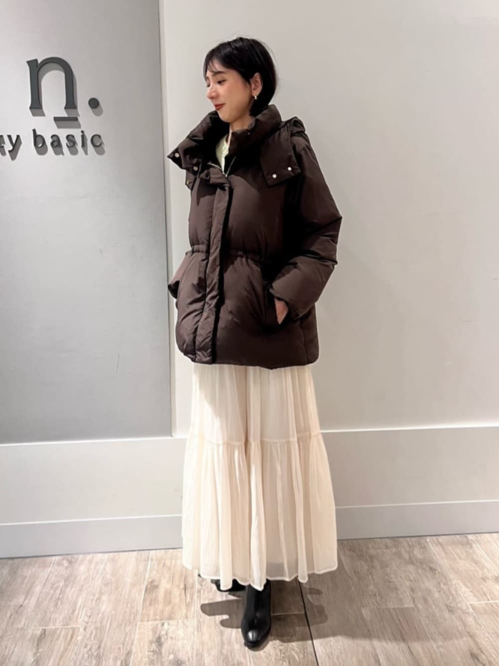 ホワイト系のスカート、グリーン系のニット/セーター、ブラウン系のダウンジャケット/コートを着用したレディースの冬コーディネートの2枚目の写真