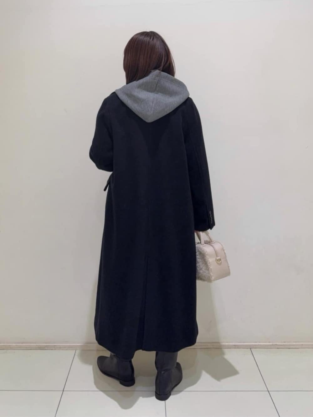 グレー系のパーカー、ブラック系のスカート、ブラック系のチェスターコートを着用したレディースの冬コーディネートの3枚目の写真