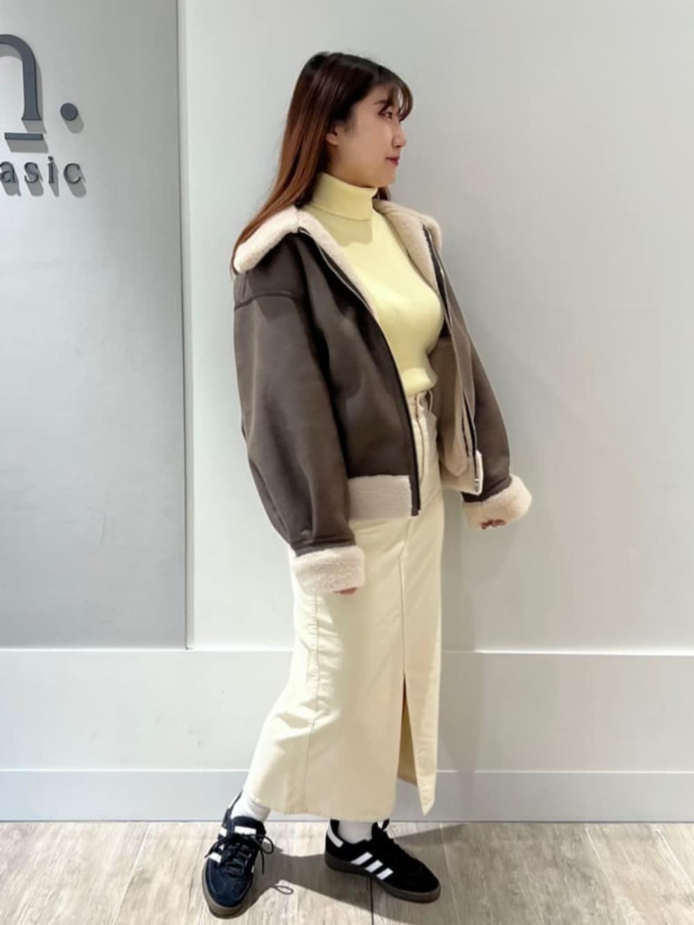 ブラウン系のブルゾン、イエロー系のニット/セーター、ホワイト系のスカートを着用したレディースの冬コーディネートの2枚目の写真