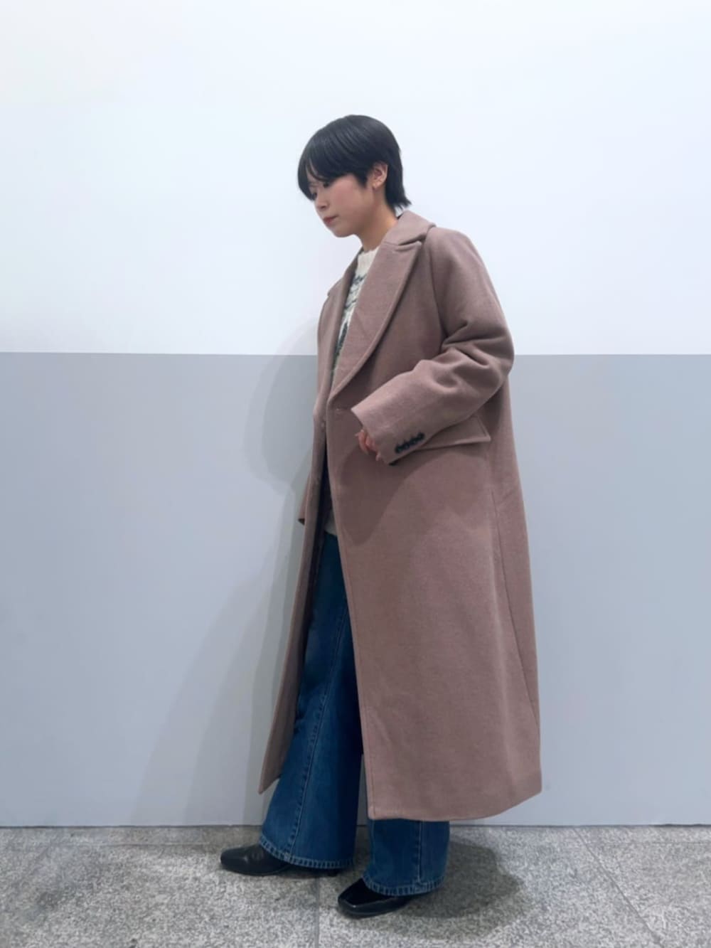 ブラウン系のチェスターコート、ホワイト系のニット/セーター、ブルー系のデニムパンツを着用したレディースの冬コーディネートの2枚目の写真