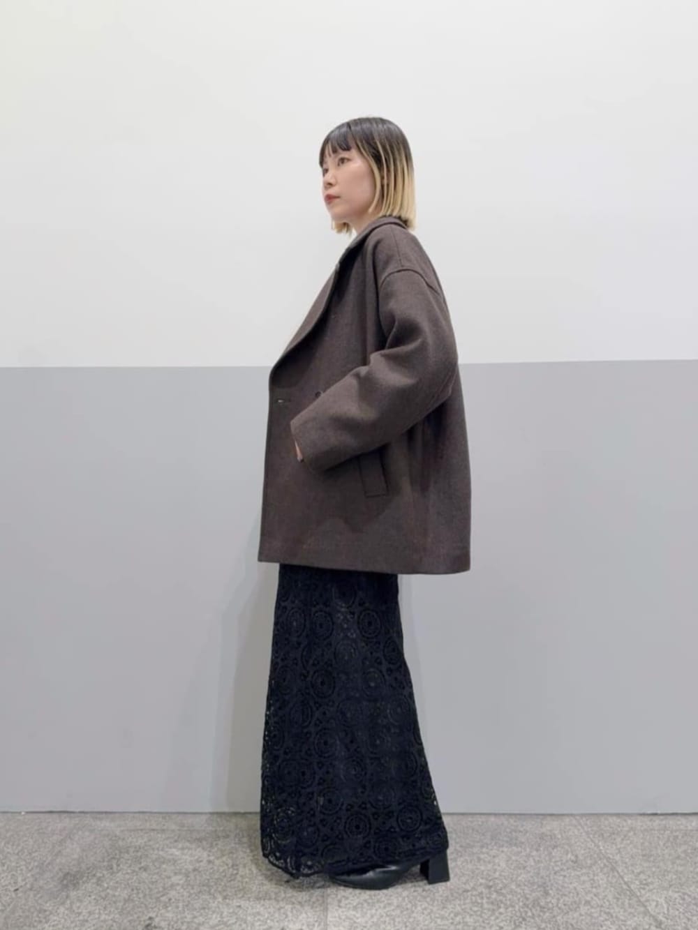 ブラウン系のピーコート、ブラック系のスカートを着用したレディースの冬コーディネートの2枚目の写真