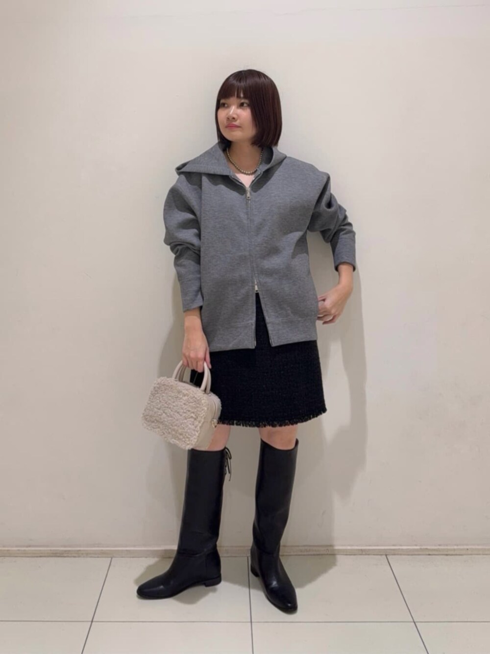 グレー系のパーカー、ブラック系のスカート、ブラック系のチェスターコートを着用したレディースの冬コーディネートの4枚目の写真