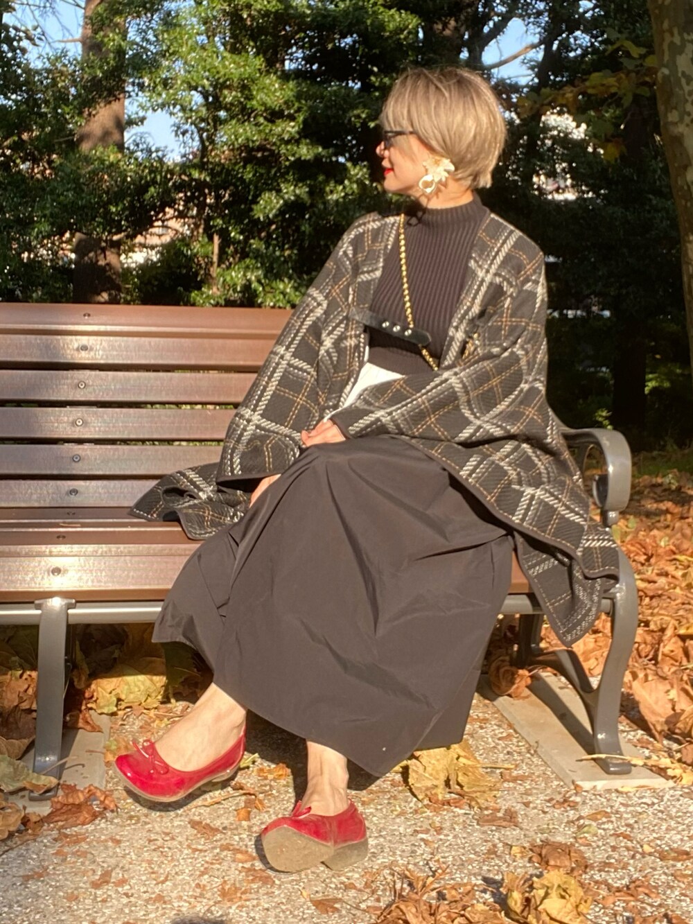 レッド系のパンプス、ブラック系のニット/セーター、ブラック系のポンチョを着用したレディースの秋コーディネートの2枚目の写真