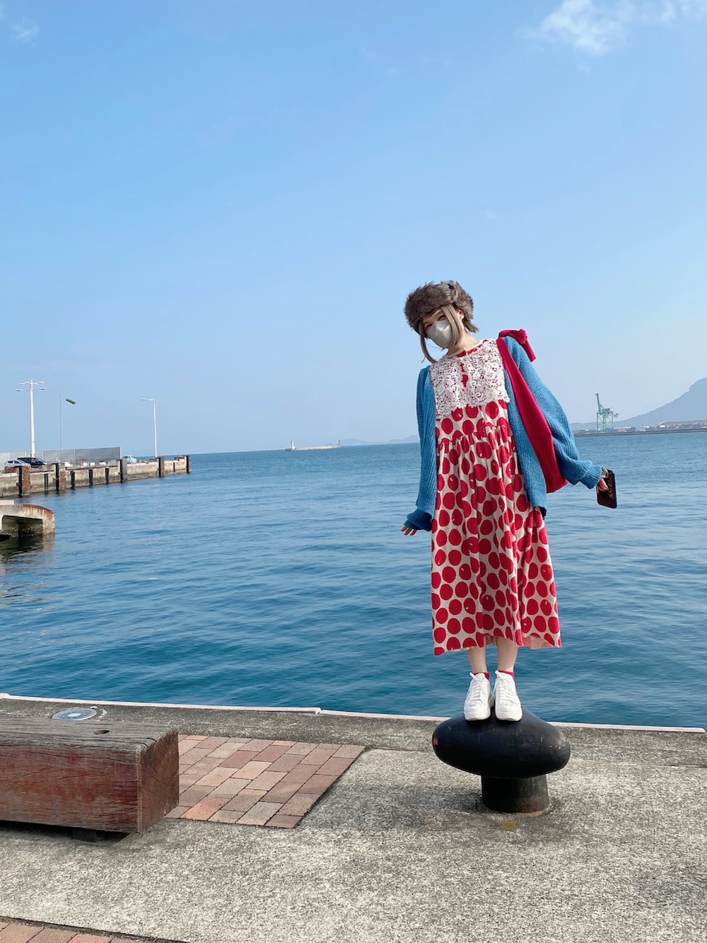 レッド系のワンピース、ブルー系のカーディガン/ボレロ、ホワイト系のスニーカーを着用したレディースの冬コーディネートの2枚目の写真