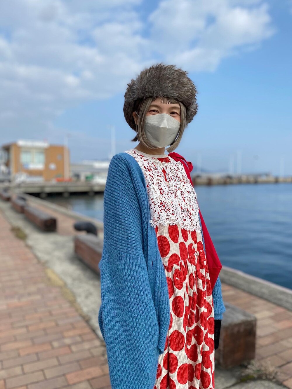 レッド系のワンピース、ブルー系のカーディガン/ボレロ、ホワイト系のスニーカーを着用したレディースの冬コーディネートの3枚目の写真