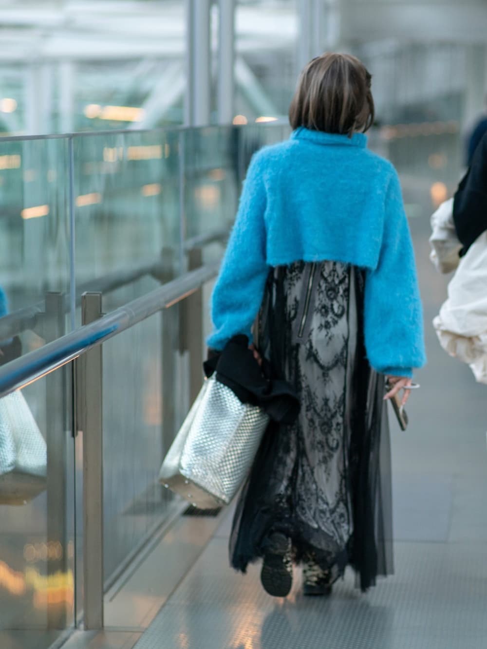 シルバー系のバッグ、ブラック系のステンカラーコート、ブラック系のワンピースを着用したレディースの冬コーディネートの3枚目の写真