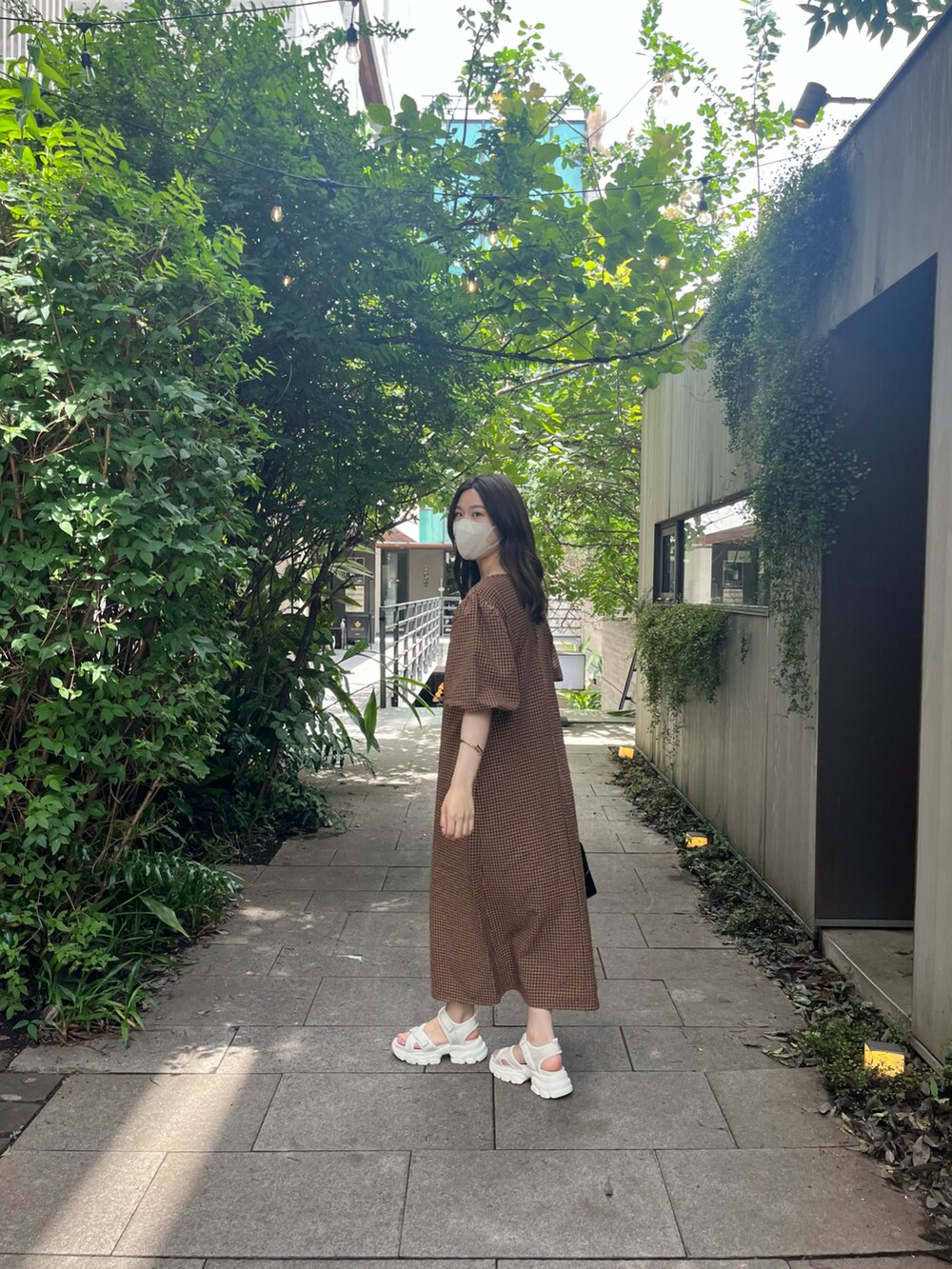 ブラック系のハンドバッグ、オレンジ系のワンピース、ベージュ系のサンダルを着用したレディースの夏コーディネートの4枚目の写真