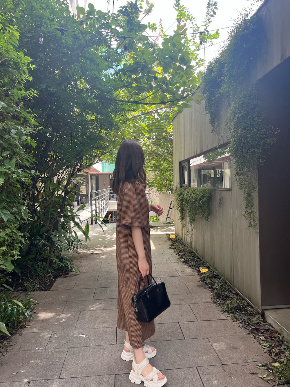 ブラック系のハンドバッグ、オレンジ系のワンピース、ベージュ系のサンダルを着用したレディースの夏コーディネートの3枚目の写真