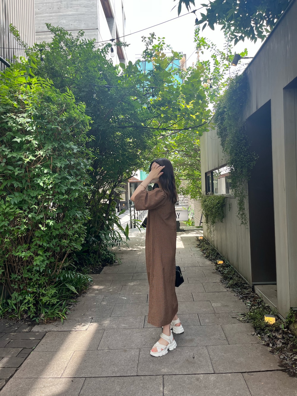 ブラック系のハンドバッグ、オレンジ系のワンピース、ベージュ系のサンダルを着用したレディースの夏コーディネートの5枚目の写真