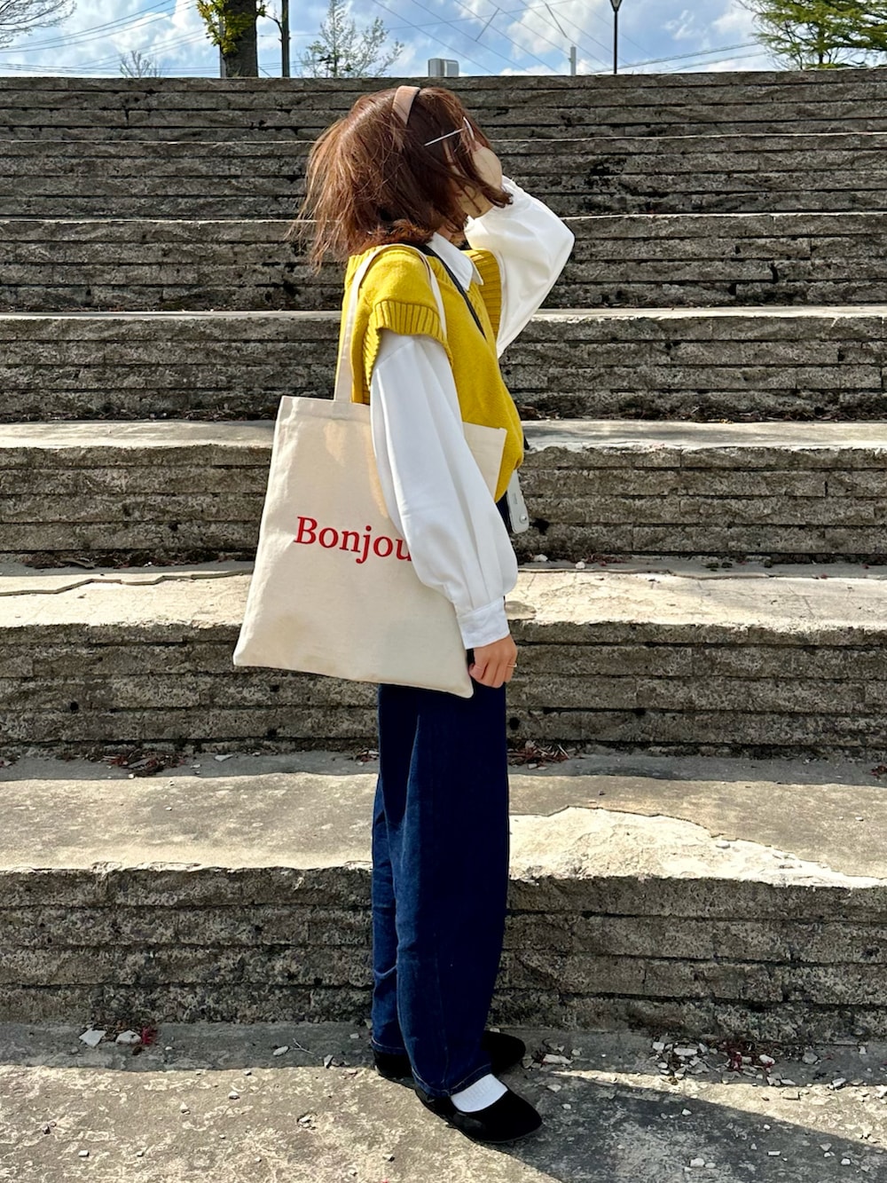 イエロー系のベスト、ブルー系のデニムパンツ、レッド系のトートバッグを着用したレディースの春コーディネートの2枚目の写真