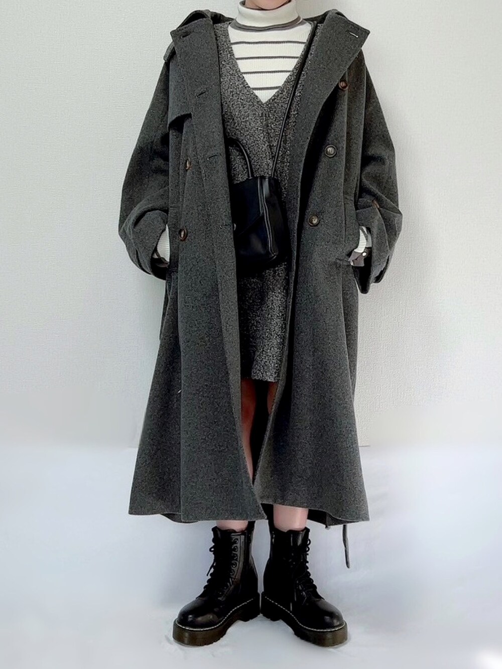 グレー系のチェスターコート、ブラウン系のニット/セーター、ブラウン系のジャンパースカートを着用したレディースの冬コーディネートの2枚目の写真