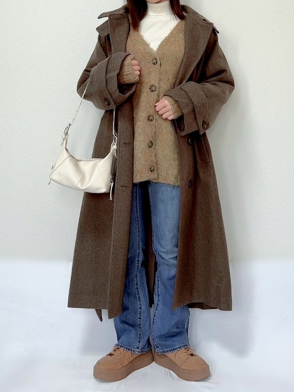 ブラウン系のステンカラーコート、グリーン系のカーディガン/ボレロ、ブラウン系のニット/セーターを着用したレディースの冬コーディネートの2枚目の写真