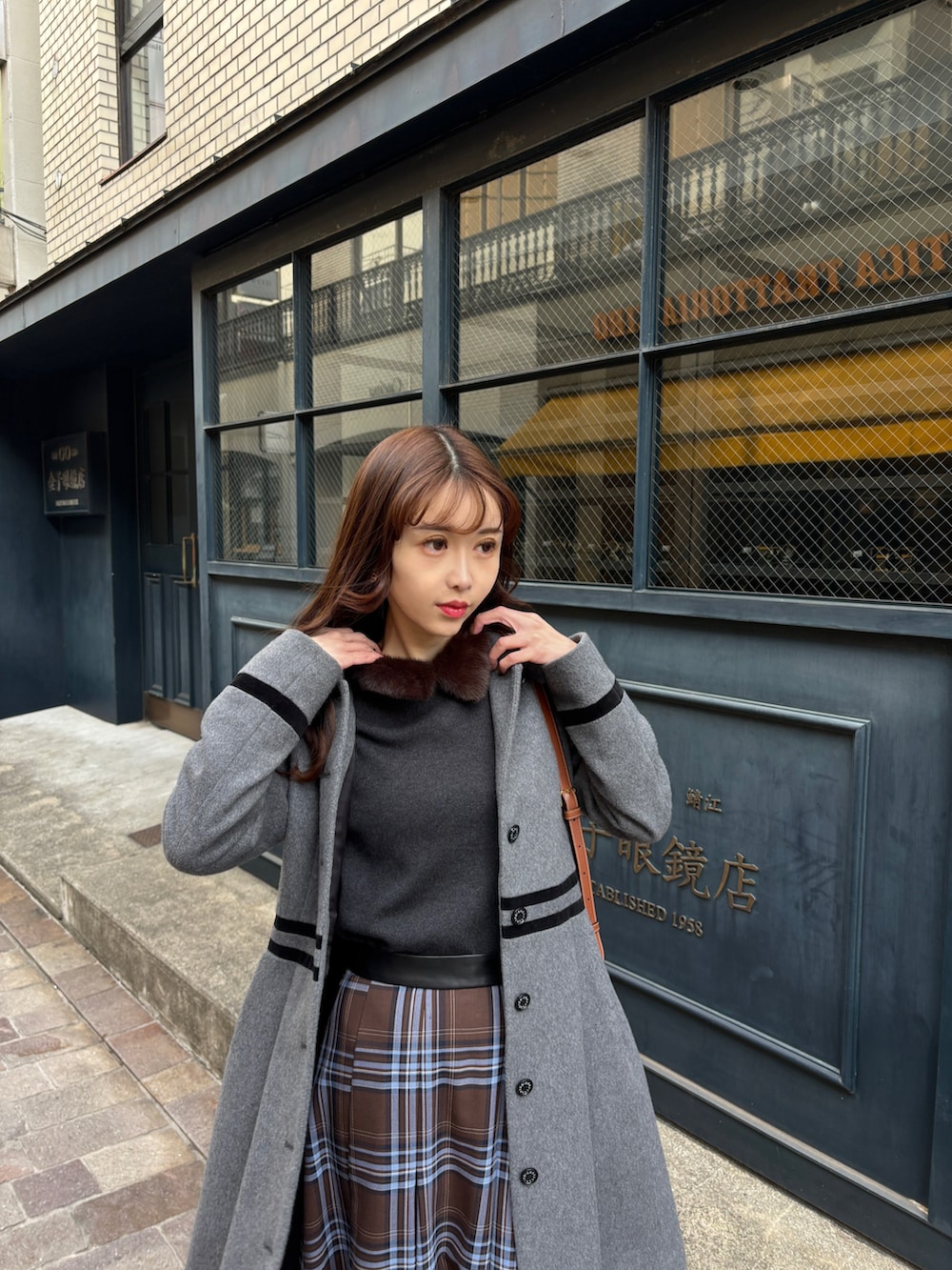 グレー系のステンカラーコート、ブラウン系のスカート、ブラック系のブーツを着用したレディースの冬コーディネートの4枚目の写真
