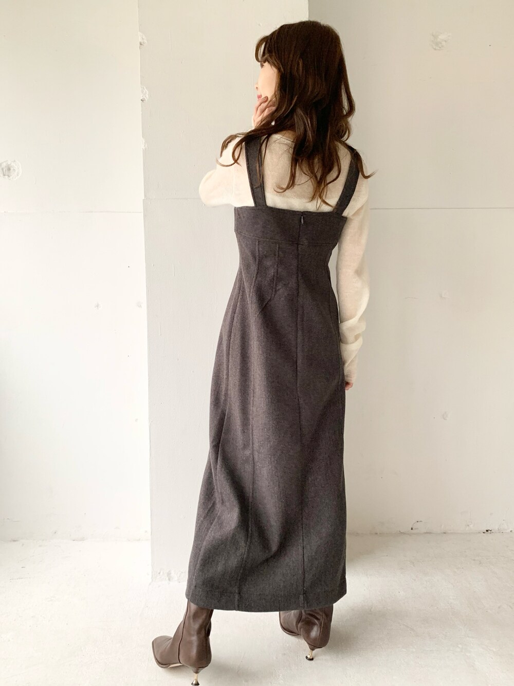 グレー系のジャンパースカート、ホワイト系のニット/セーター、ブラウン系のブーツを着用したレディースの秋コーディネートの2枚目の写真