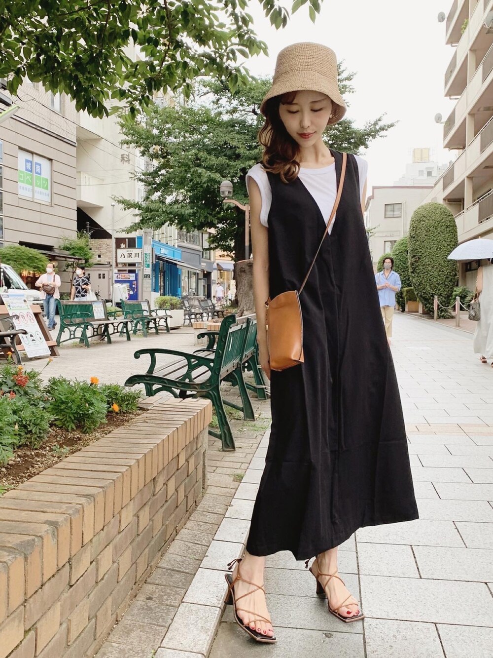 ブラック系のジャンパースカート、ホワイト系のTシャツ/カットソー、ブラウン系のサンダルを着用したレディースの夏コーディネートの2枚目の写真