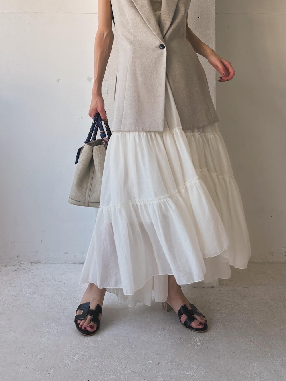 ホワイト系のスカート、ベージュ系のベスト、ブラック系のサンダルを着用したレディースの夏コーディネートの3枚目の写真