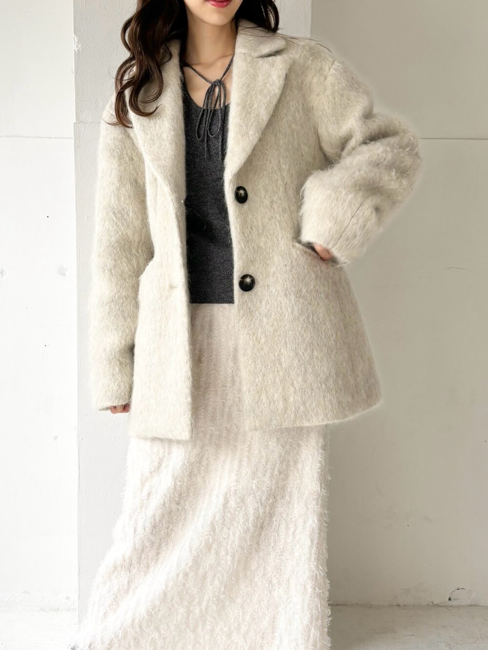 グレー系のチェスターコート、グレー系のニット/セーター、ホワイト系のスカートを着用したレディースの冬コーディネートの2枚目の写真