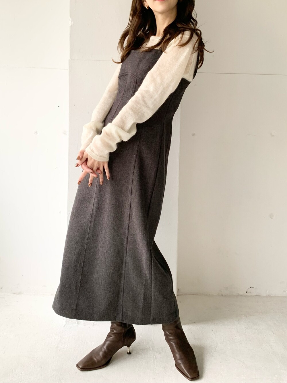 グレー系のジャンパースカート、ホワイト系のニット/セーター、ブラウン系のブーツを着用したレディースの秋コーディネートの3枚目の写真