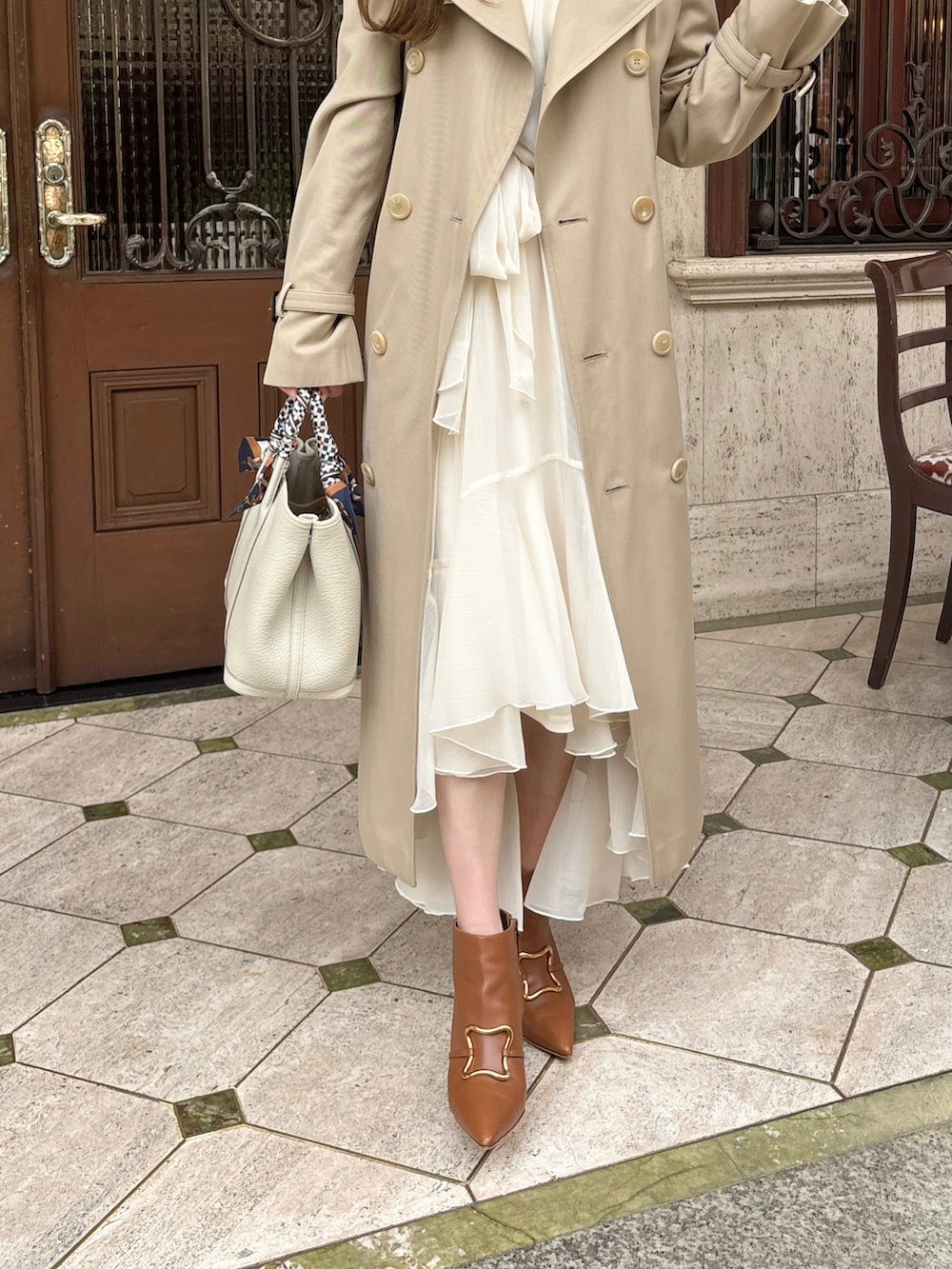 ホワイト系のワンピース、ブラウン系のブーツ、ベージュ系のトレンチコートを着用したレディースの春コーディネートの2枚目の写真