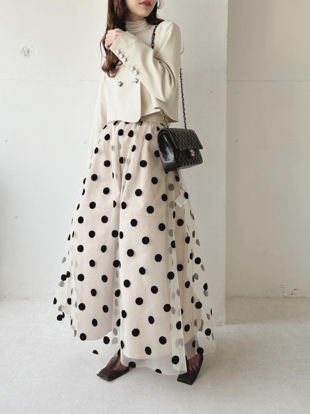 ベージュ系のノーカラージャケット、ベージュ系のスカート、ブラウン系のブーツを着用したレディースの春コーディネートの2枚目の写真