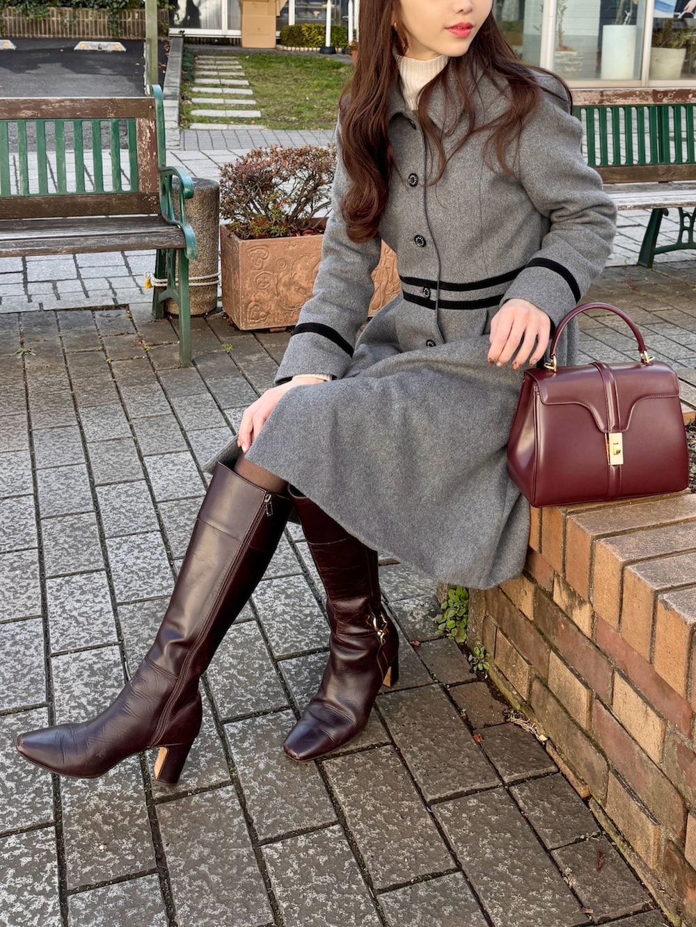 グレー系のステンカラーコート、ブラウン系のブーツ、レッド系のバッグを着用したレディースの冬コーディネートの3枚目の写真
