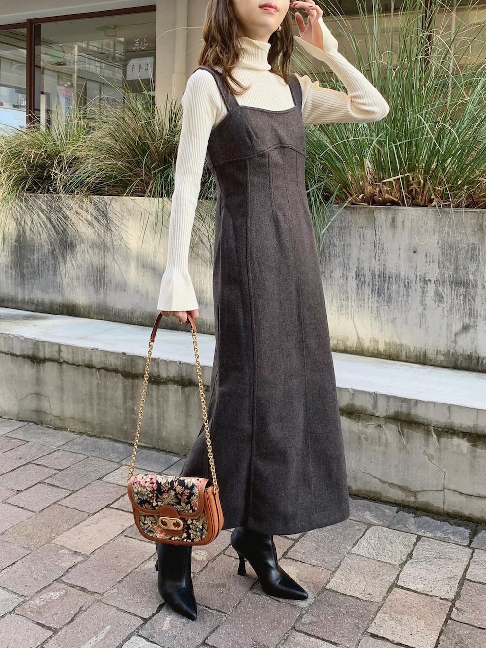 グレー系のジャンパースカート、ブラウン系のバッグ、ブラック系のブーツを着用したレディースの秋コーディネートの2枚目の写真