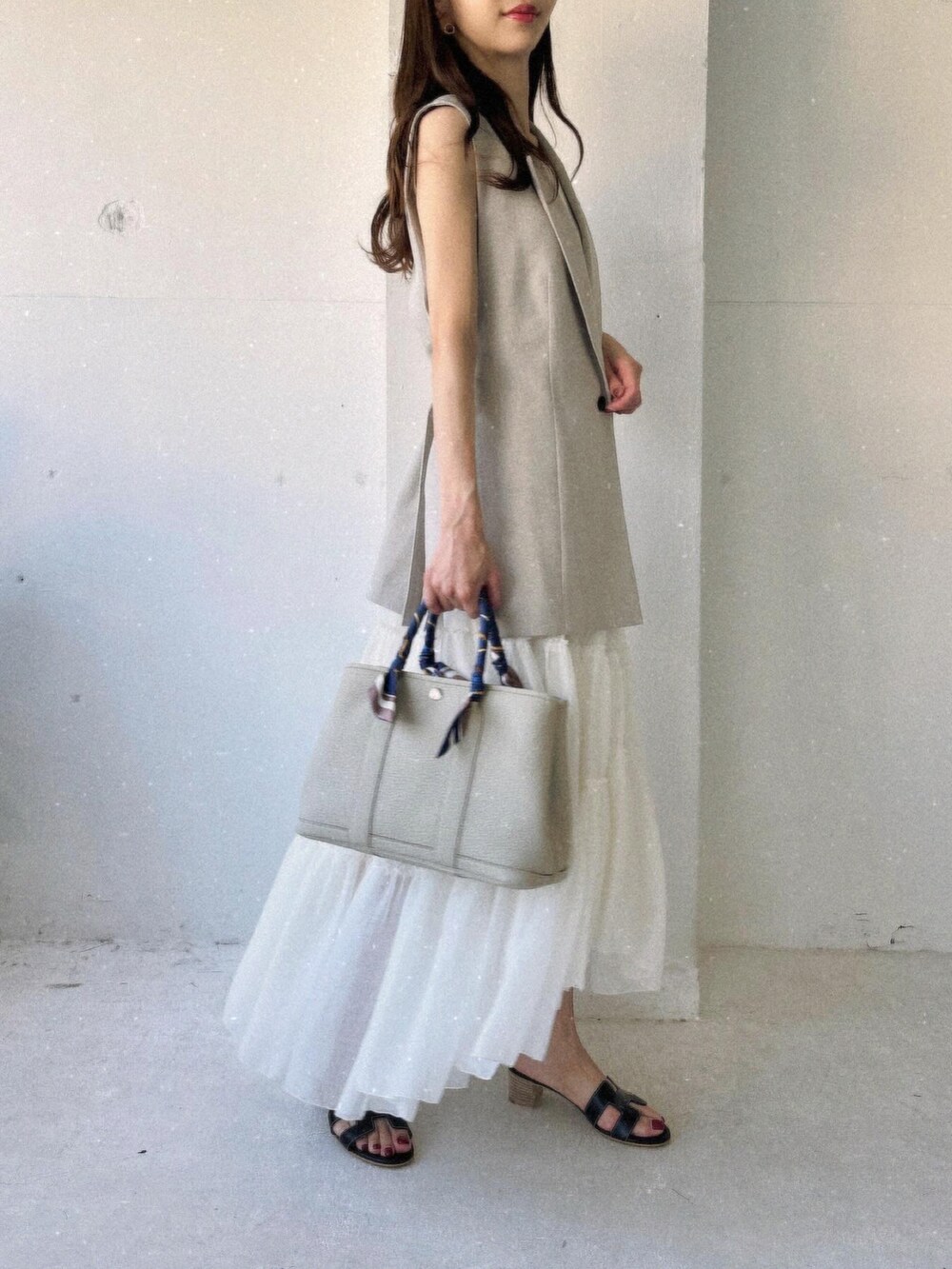 ホワイト系のスカート、ベージュ系のベスト、ブラック系のサンダルを着用したレディースの夏コーディネートの2枚目の写真