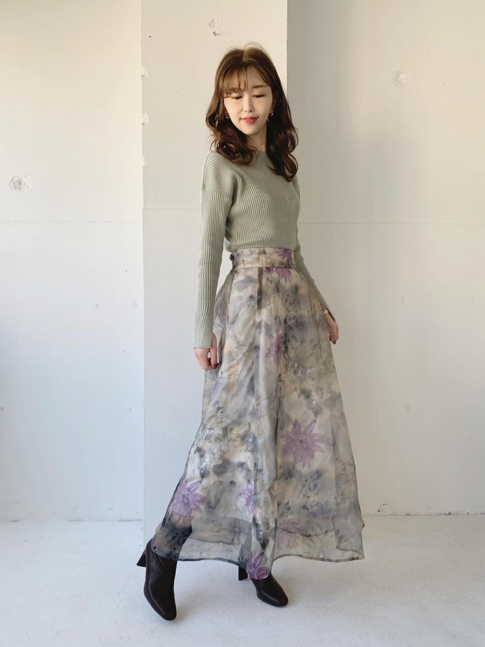 グリーン系のニット/セーター、グレー系のスカート、ブラウン系のブーツを着用したレディースの冬コーディネートの2枚目の写真