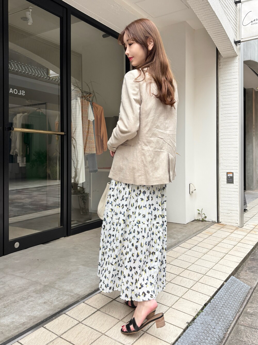 ベージュ系のテーラードジャケット、ホワイト系のワンピース、ブラック系のサンダルを着用したレディースの春コーディネートの3枚目の写真