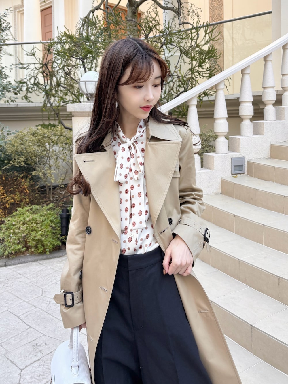 ベージュ系のトレンチコート、ベージュ系のバッグ、ブルー系のその他パンツを着用したレディースの冬コーディネートの2枚目の写真