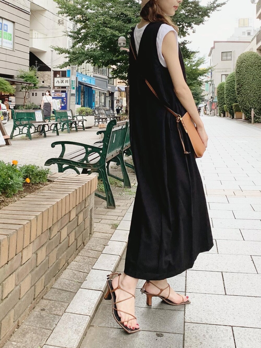 ブラック系のジャンパースカート、ホワイト系のTシャツ/カットソー、ブラウン系のサンダルを着用したレディースの夏コーディネートの3枚目の写真