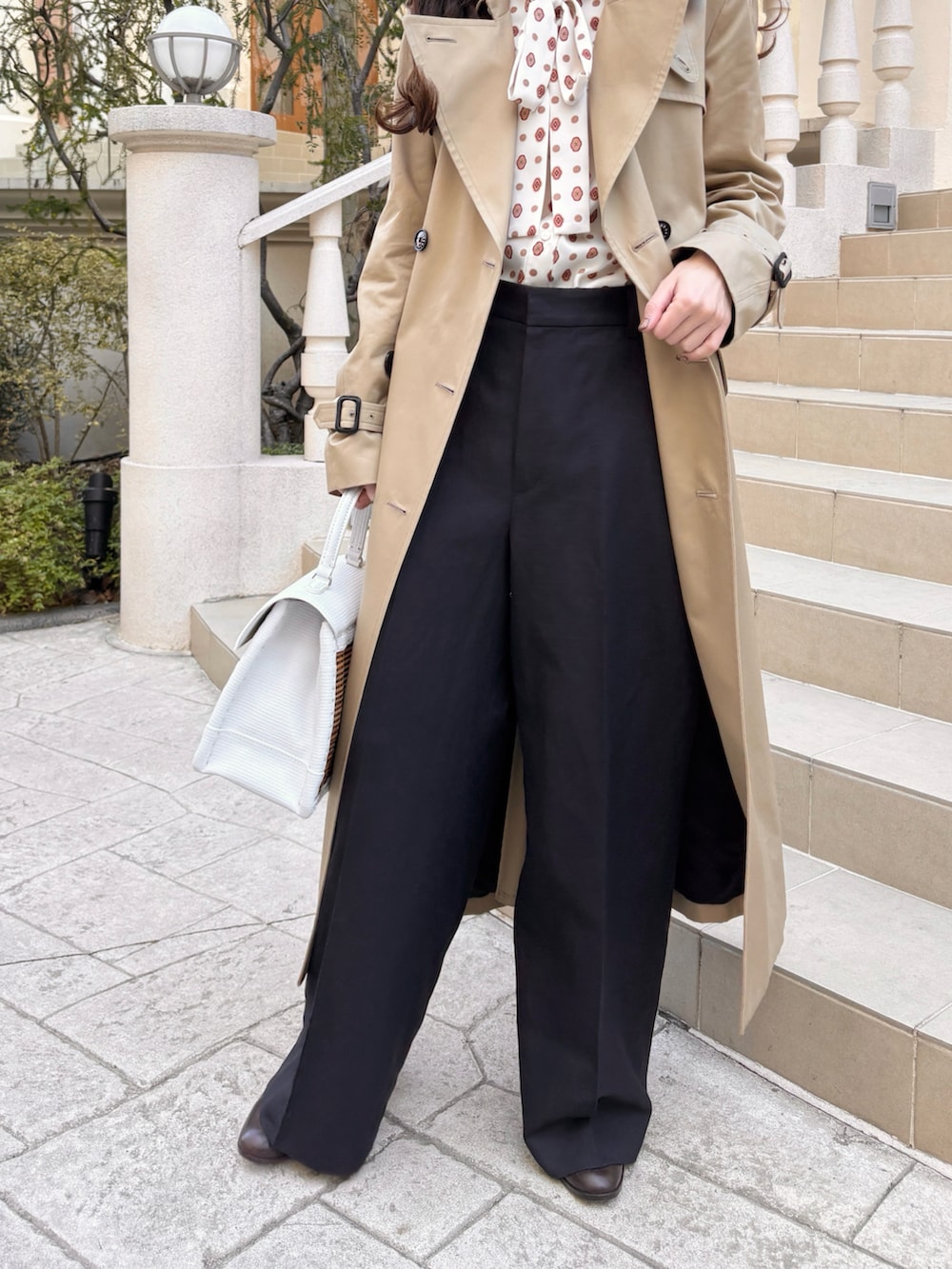 ベージュ系のトレンチコート、ベージュ系のバッグ、ブルー系のその他パンツを着用したレディースの冬コーディネートの3枚目の写真