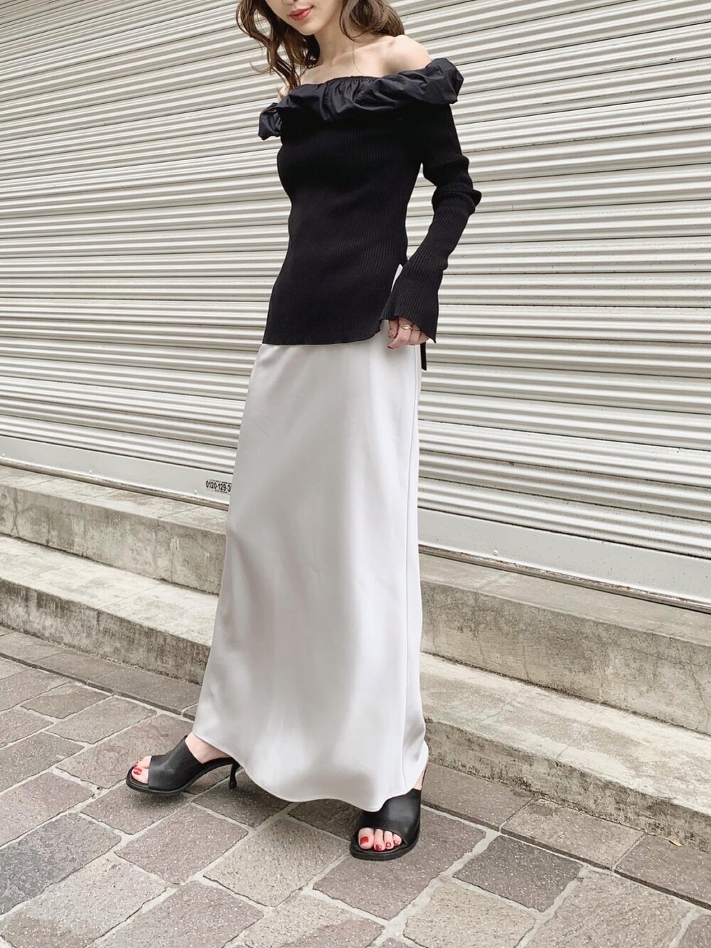 ブラック系のニット/セーター、グレー系のスカート、ブラック系のサンダルを着用したレディースの春コーディネートの2枚目の写真