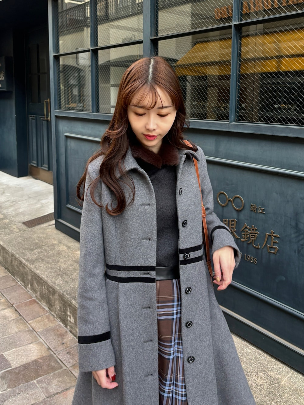 グレー系のステンカラーコート、ブラウン系のスカート、ブラック系のブーツを着用したレディースの冬コーディネートの3枚目の写真