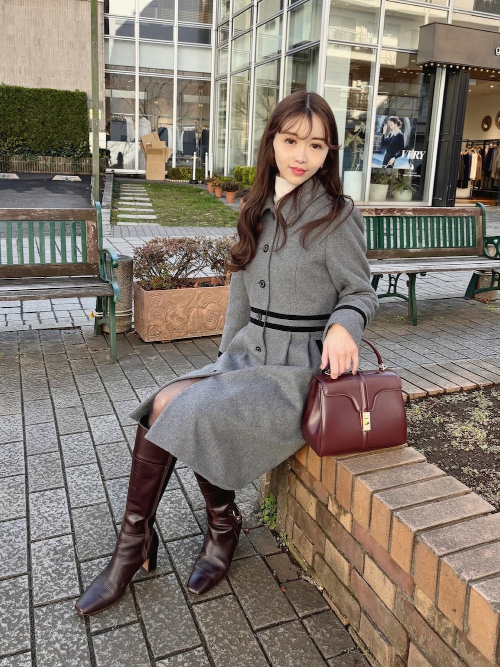 グレー系のステンカラーコート、ブラウン系のブーツ、レッド系のバッグを着用したレディースの冬コーディネートの2枚目の写真