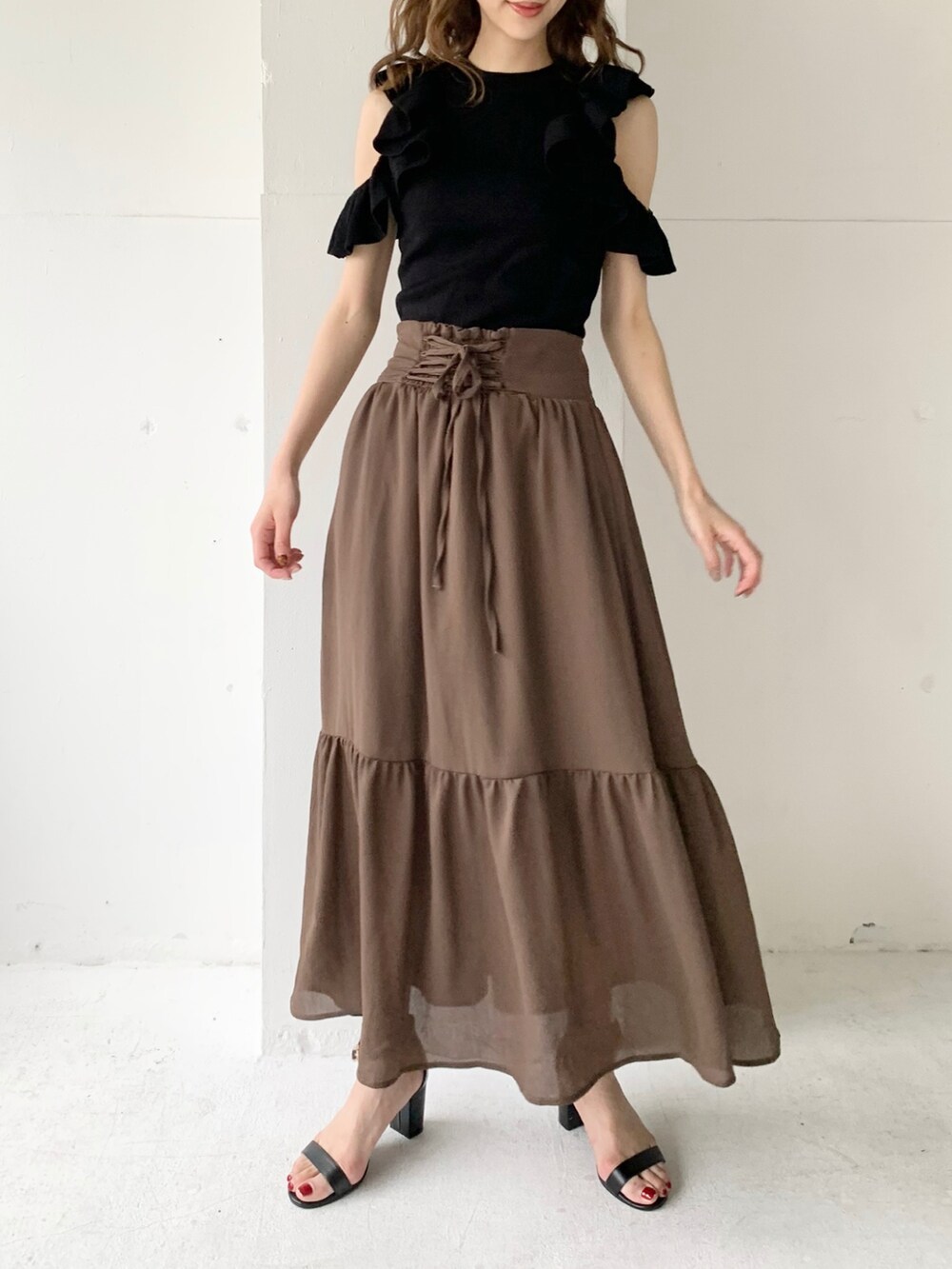 ブラウン系のスカート、ブラック系のニット/セーター、ブラック系のサンダルを着用したレディースの夏コーディネートの2枚目の写真