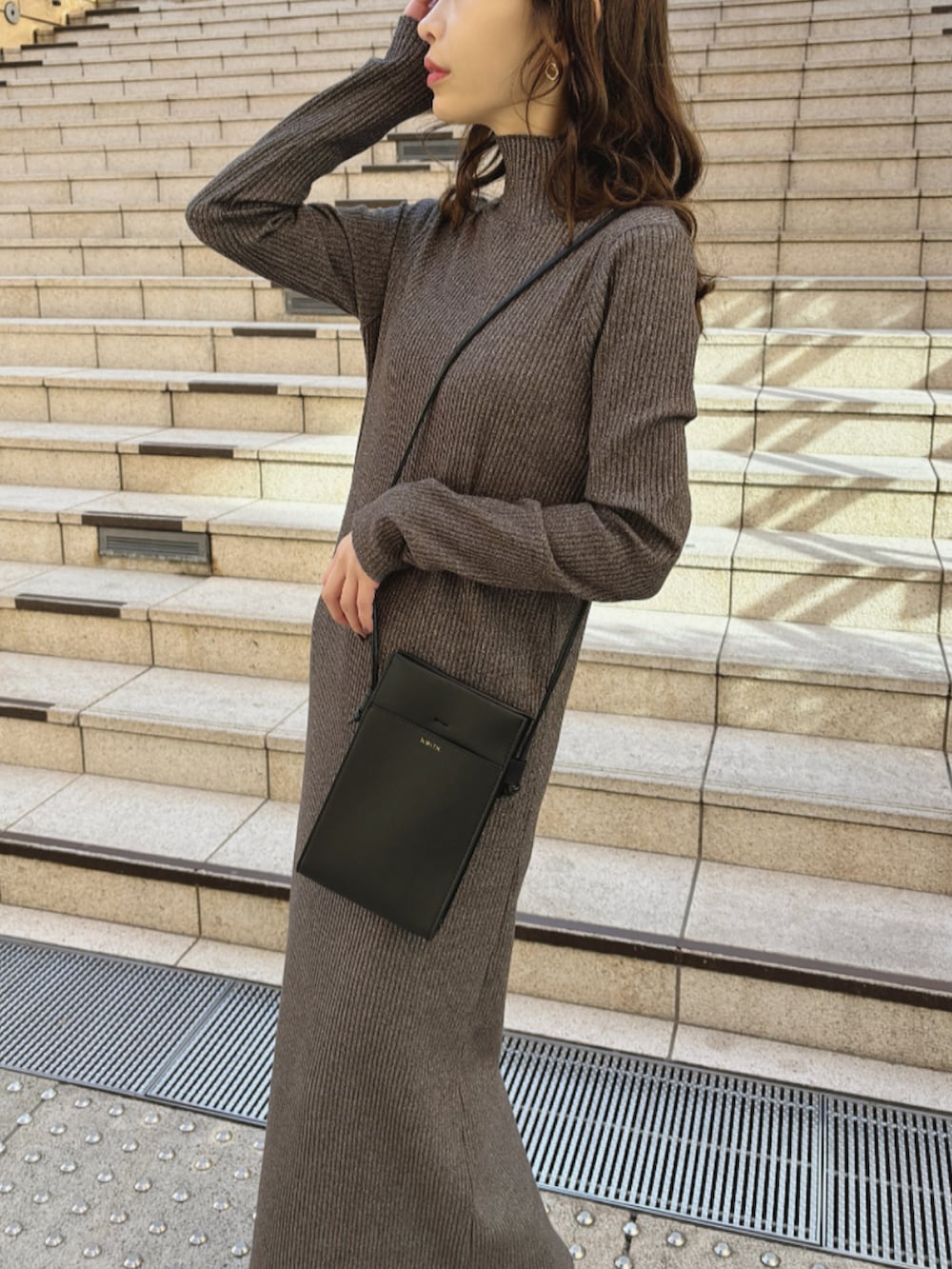 グレー系のワンピース、ブラック系のショルダーバッグ、ブラウン系のブーツを着用したレディースの冬コーディネートの2枚目の写真