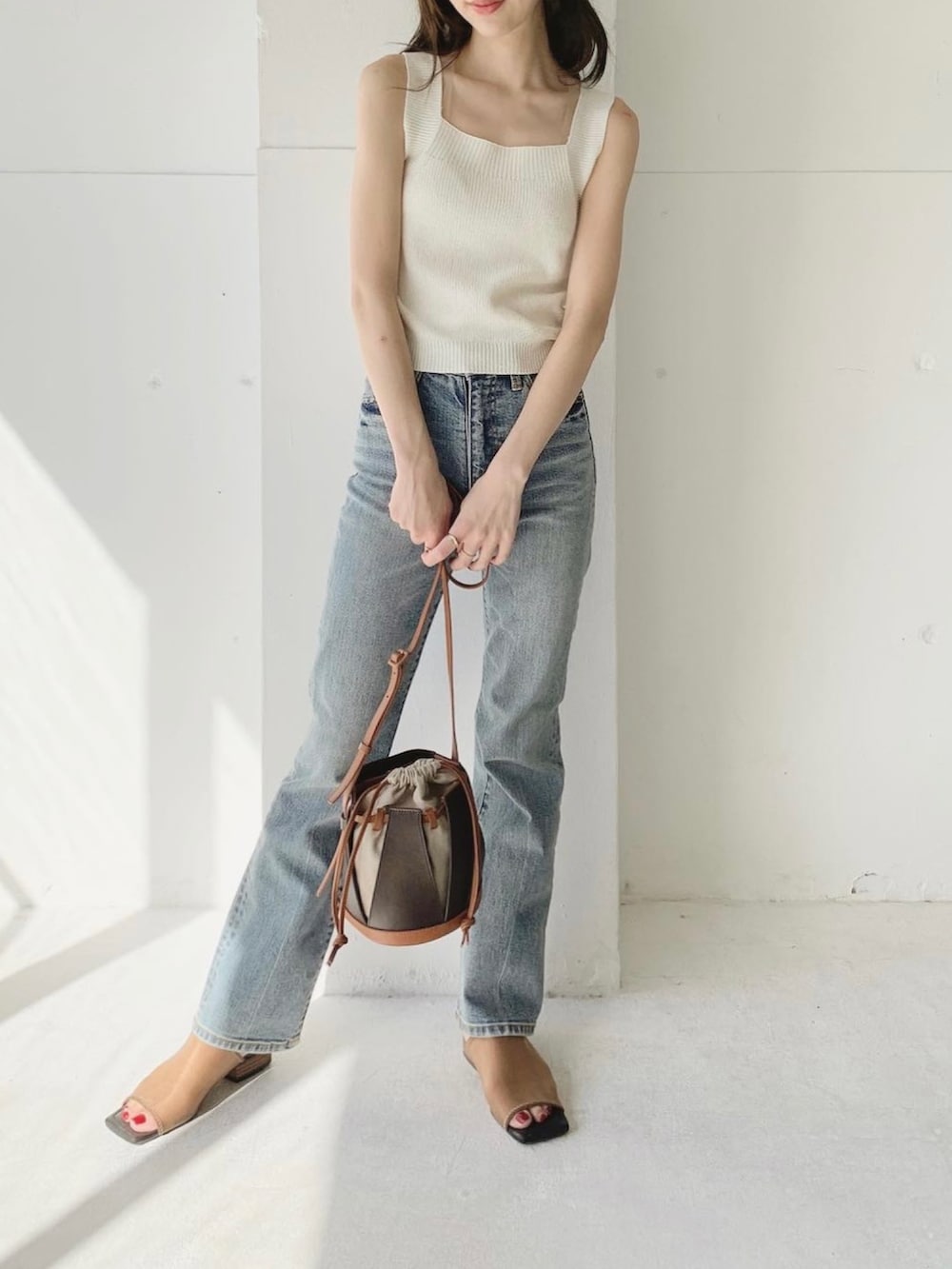ホワイト系のタンクトップ、ブルー系のデニムパンツ、ブラウン系のショルダーバッグを着用したレディースの夏コーディネートの2枚目の写真